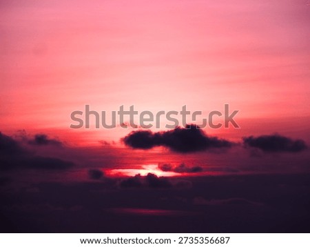 A breathtaking sunset ignites the sky with deep shades of magenta and crimson. Dark, heavy clouds drift across the horizon, partially veiling the glowing sun as it casts a final, radiant light through the dramatic evening atmosphere.