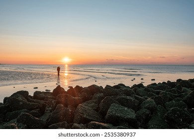 A breathtaking sunset illuminates the calm beach with its rocky shoreline and gentle waves lapping the shore - Powered by Shutterstock