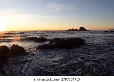 Breathtaking sunset over Ruby Beach in the Olympic Coast National Marine Sanctuary, Washington State, with the last golden light of day casting warm orange and blue tones across the sky and the vast Pacific Ocean. Iconic sea stacks  along black sand shoreline create a dramatic foreground as waves wash gently across the beach in the fading light. Located within Olympic National Park on the wild Pacific Northwest coast, Ruby Beach is one of the most photographed and celebrated coastal landscapes in the United States. The rugged offshore rock formations silhouetted against the glowing sky make this a powerful and emotive image ideal for travel, conservation, nature, Pacific Northwest, and USA destination content.