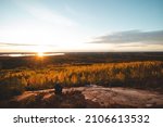 Breathtaking sunset from a rock near Paltamo, Finland. An adventurer rests on a rock and watches an orange orb illuminate the coloured leaves of the trees. Autumn colours.