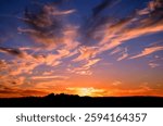 A breathtaking sunset sky over the Kata Tjuta rock formations, of purple, orange, and yellow. The massive rock domes stand silhouetted against the fiery colors. 