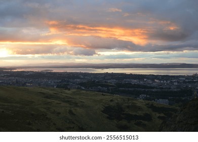 A breathtaking sunset view over Edinburgh, featuring dramatic skies, rolling hills, and the Firth of Forth shimmering in the background - Powered by Shutterstock