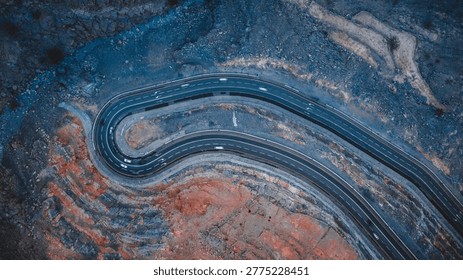 Breathtaking top-down aerial view of a dramatic hairpin bend on Jebel Jais mountain road in Ras Al Khaimah, UAE, carved into striking red and grey rocky terrain