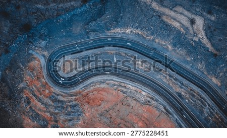 Breathtaking top-down aerial view of a dramatic hairpin bend on Jebel Jais mountain road in Ras Al Khaimah, UAE, carved into striking red and grey rocky terrain