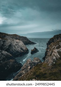 A breathtaking view of Anglesey's rugged cliffs, towering over the crashing waves of the Irish Sea. The vibrant green grass contrasts beautifully with the deep blue waters.