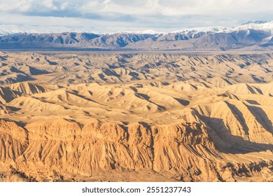 A breathtaking view of an arid landscape featuring intricate patterns of rugged hills and golden ridges illuminated by sunlight. The foreground highlights dramatic red rock formations  - Powered by Shutterstock