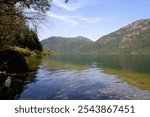 Breathtaking view of Cameron Lake with blue-green waters, surrounded by majestic mountains and a clear blue sky, Vancouver Island, BC