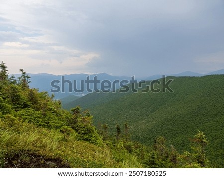 A breathtaking view from Cascade Mountain's summit, where rays of light pierce through heavy clouds, illuminating the Adirondacks in New York State.