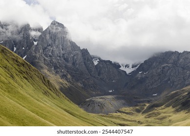 A breathtaking view of the Caucasus Mountains in Georgia during autumn, showcasing rugged peaks, scattered snow patches, and vibrant green valleys under a cloudy daytime sky - Powered by Shutterstock