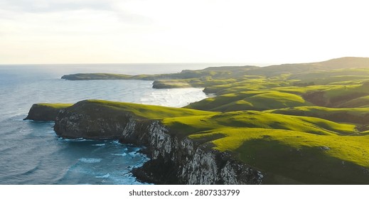 A breathtaking view of dramatic coastal cliffs covered in vibrant green grass, meeting the deep blue ocean waves