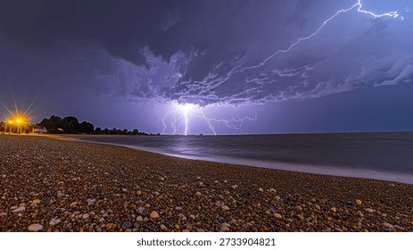 Breathtaking view of a dramatic lightning storm occurring over a pebble beach at night. The powerful lightning illuminates the dark clouds against the horizon, creating a striking contrast with the tranquil waters of the sea and the textured pebble beach.