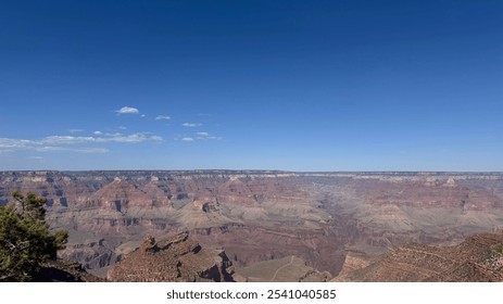 Breathtaking view of the Grand Canyon from a cliff edge, showcasing rugged mountains, rocky terrain, and scattered trees under a clear blue sky in Arizona. Nature at its finest - Powered by Shutterstock