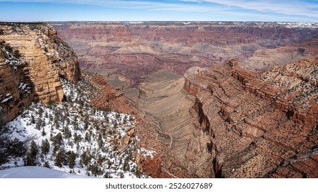 A breathtaking view of the Grand Canyon showcases its vast, layered rock formations under a clear sky. Snow dusts the tops of the cliffs, contrasting with the rich reds and browns of the stone. - Powered by Shutterstock