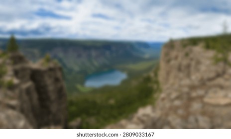 A breathtaking view from a high vantage point overlooking a deep canyon with a serene turquoise lake nestled within the lush green landscape, under a dynamic cloudy sky.