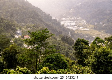 A breathtaking view of a misty mountain valley. Lush green forests blanket the slopes, dotted with small houses and a winding road. The mist adds a touch of mystery to the scene.  - Powered by Shutterstock