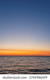 A breathtaking view of the ocean at sunset, featuring a seamless blend of orange and blue hues as the day transitions to night. the calm water reflects the sky's vibrant colors, creating a peaceful and serene atmosphere.