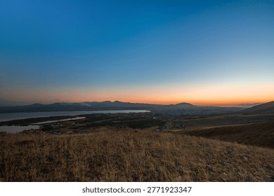 A breathtaking view over the Sevan valley at sunset, with orange skies fading into deep blue above the lake and the silhouettes of mountains in the distance.
