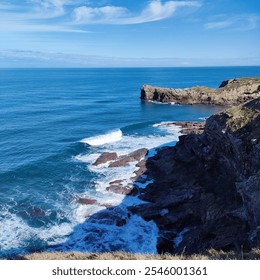 A breathtaking view of rocky cliffs meeting the blue ocean waves, under a clear sky with wispy clouds, capturing the serenity of coastal nature and landscape. - Powered by Shutterstock