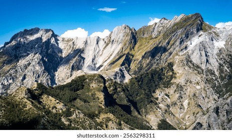 A breathtaking view of rugged mountains under a clear blue sky, showcasing steep cliffs and rocky peaks with patches of greenery at the base. - Powered by Shutterstock