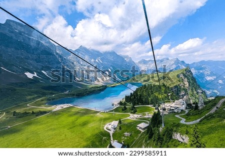 Breathtaking view of a serene lake nestled atop Mount Titlis. The lake itself is calm and tranquil, with clear, still waters that reflect the surrounding mountains and sky.