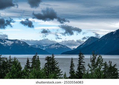 A breathtaking view of a serene lake surrounded by majestic snow-capped mountains and lush green trees under a partly cloudy sky. - Powered by Shutterstock