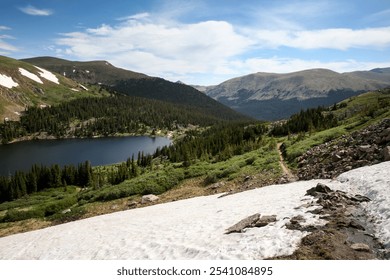 A breathtaking view of a serene mountain lake surrounded by lush greenery and snow-capped peaks under a clear blue sky - Powered by Shutterstock