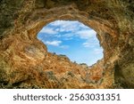 A breathtaking view of the skylight in Benagil Cave, showcasing the natural rock formations and the blue sky above. This famous sea cave is known for its unique beauty. Algarve, Portugal.