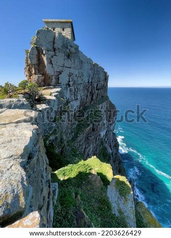 A breathtaking view of a small structure on top of a sheer stone cliff cutting into the blue sea below at Cape Point.