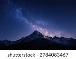 A breathtaking view of a snow-capped mountain range silhouetted against a vibrant night sky filled with the Milky Way and countless stars.