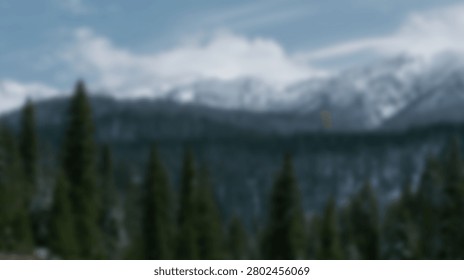 A breathtaking view of a snow-capped mountain range towering over a dense evergreen forest, under a cloudy sky.
