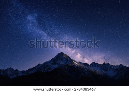 A breathtaking view of a snow-capped mountain range silhouetted against a vibrant night sky filled with the Milky Way and countless stars.