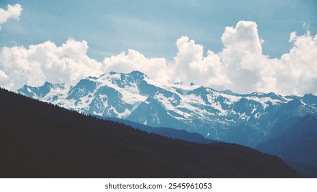 A breathtaking view of snow-capped mountains against a backdrop of a clear blue sky with fluffy clouds. The serene beauty of nature, the grandeur of the mountain range and the tranquility of the scene - Powered by Shutterstock