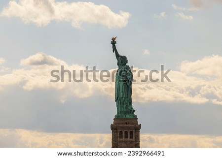 Breathtaking view of Statue of Liberty on Liberty Island in New York set against backdrop of pale blue sky with white clouds.