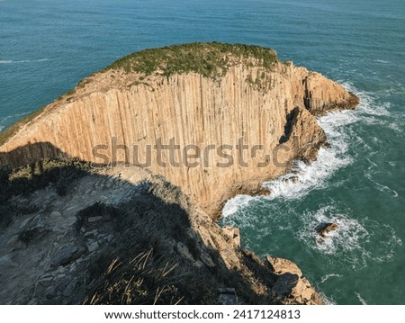 A breathtaking view of a steep cliff that juts out into the ocean. The cliff has distinct vertical striations, showcasing its geological features and texture.