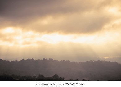 A breathtaking view of sun rays piercing through thick clouds, illuminating the misty mountain range below. - Powered by Shutterstock