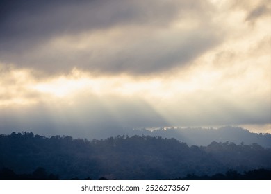 A breathtaking view of sun rays piercing through thick clouds, illuminating the misty mountain range below. - Powered by Shutterstock