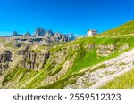 Breathtaking view of tre cime di lavaredo peaks in the italian dolomites, featuring a picturesque alpine hut amidst lush greenery under a vibrant blue sky