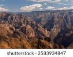 A breathtaking view of a vast Copper Canyon landscape with rugged cliffs and deep valleys under a blue sky with fluffy clouds.