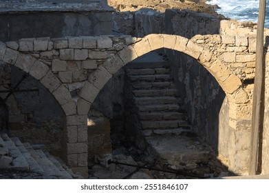 A breathtaking view of weathered stone arches leading to narrow stairs beside the coastal ruins. - Powered by Shutterstock