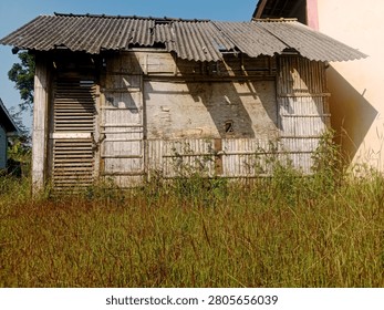Brebes, Central Java, July 3, 2026. This photo shows an old house that appears to have been unoccupied for a long time. The building is made of a combination of bamboo and wooden planks that have rotted with age. The corrugated asbestos roof appears damaged, with several holes and cracks. The walls of the house show peeling paint and brittle wood surfaces.

In front of the house, weeds have grown tall, covering part of the yard, giving it a neglected appearance.