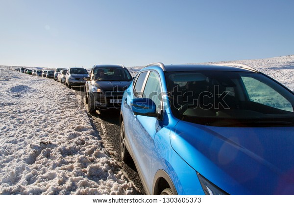 Brecon\
Beacons, UK: February 02, 2019: Cars have carelessly parked on the\
grass shoulder of a snow covered mountain road causing gridlock and\
difficulty for other cars to pass by\
safely.