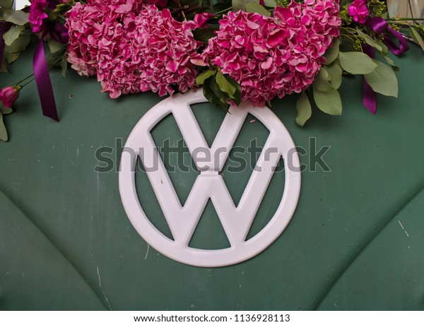 Bremen, Germany - July 17th, 2018 - Close-up\
photo of the front of a green VW T3 van with white VW logo\
decorated with pink\
flowers