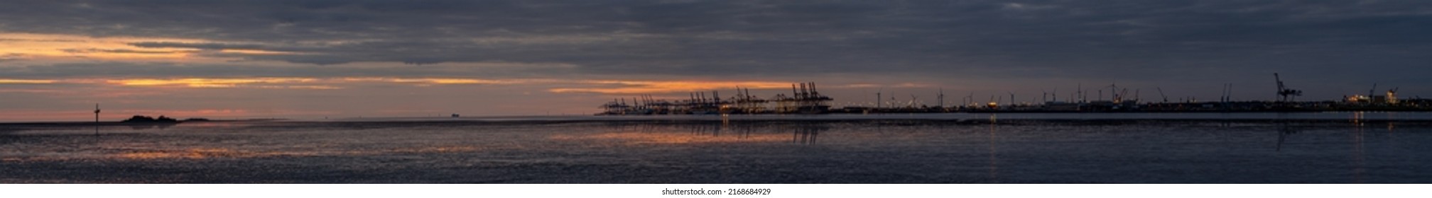 Bremerhaven, Germany - June 14, 2022: large scenic sunset panorama of the  overseas port with cranes and container ships and the silhouette of the artificial islands Langlütjen I and II