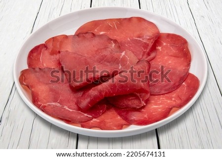 Bresaola slices in plate on white wooden table, italian dried beef salami from Valtellina