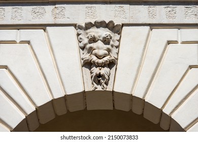 Brescia. Closeup of Medieval Broletto Palace (Palazzo Broletto or Palazzo del Governo), XII-XXI century. White stone arch with keystone and a gargoyle grotesque human mask.  Lombardy, Italy, Europe.