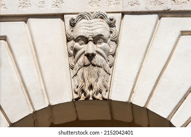 Brescia. Closeup of Medieval Broletto Palace (Palazzo Broletto or Palazzo del Governo), XII-XXI century. White stone arch with keystone and a gargoyle grotesque human mask. Lombardy, Italy, Europe.