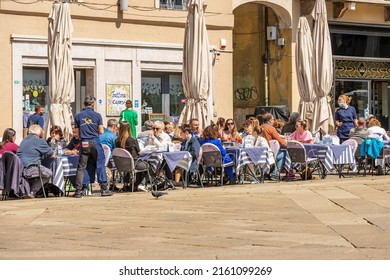 BRESCIA, ITALY - APRIL 17, 2022: Outdoor restaurant crowded with people on a sunny spring day in Brescia downtown, Loggia town square (Piazza della Loggia), Lombardy, Italy, Europe.