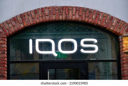 Brest, Belarus. Jun 2022. Sign IQOS Glowing In Evening. Neon Company Signboard IQOS On Shop Window. IQOS Of Philip Morris International - Boutique Of Heated Tobacco Smoking Devices. 