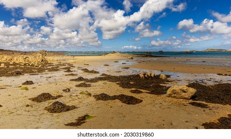 The Breton coast on the island of Bréhat during low tide, with boats and a blue sky and clouds. Brittany, France. 