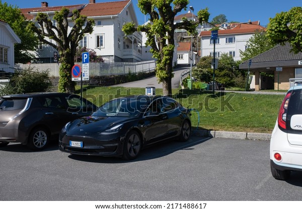 Brevik, Norway - May 26,\
2022: A static shot of a solid black Tesla Model 3 dual motor\
charging at the Recharge AC charging station in a cloudy spring\
day. Selective focus.